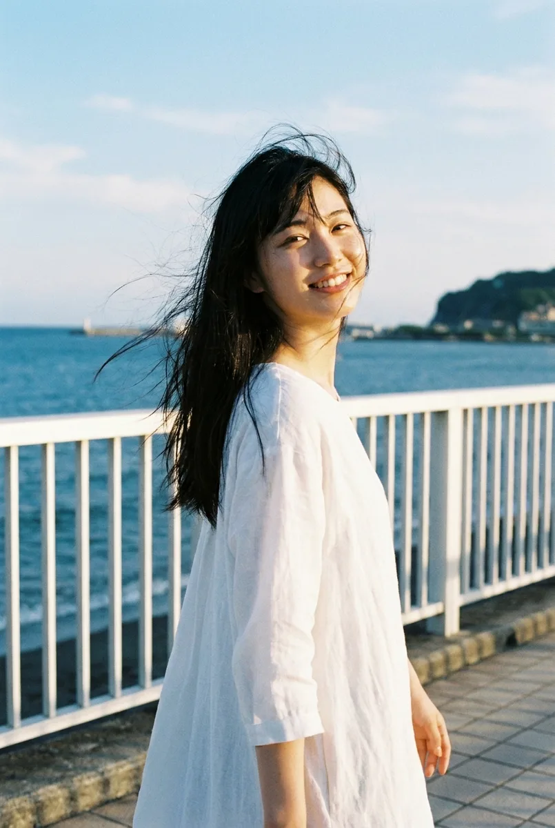 Nano Banana Proの作例（2枚目）：文章で書いた：A photorealistic waist-up photograph of … She is walking along a seaside promenade …